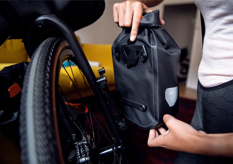 Rider clips an Ortlieb fork pack onto its quick-release bracket on the fork of a gravel bike.