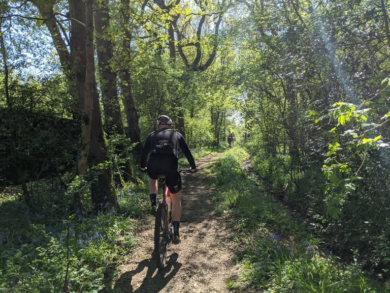 Rider follows a narrow woodland path through bluebells on the Bristol Green Belt 360, a horse rider ahead.