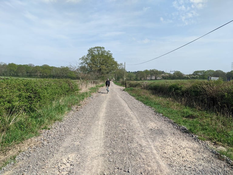 Cyclist rides away along a wide gravel track between hedges and fields on the north side of Bristol.