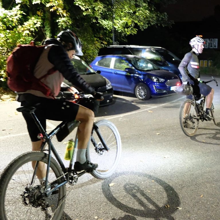 Two riders with lights on in a car park at night during the Great British Escapade on the North and South Downs.