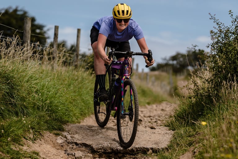 Smiling rider in a yellow helmet rolls a gravel bike down a rocky slab of track while testing WTB SG2 tyres.