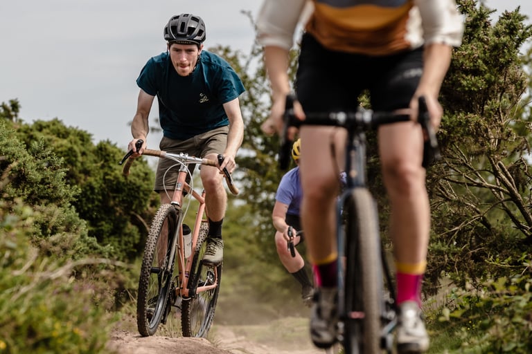 Three riders testing WTB SG2 tyres on a dusty, rocky track between gorse bushes in the Mendip Hills.