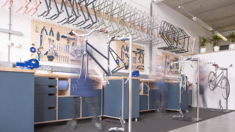 Temple Cycles workshop in Bristol with frames on racks, tool boards and blurred mechanics at work.