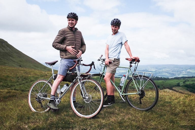 Temple Cycles founder Matt Mears and a friend stand with their Temple bikes on a grassy hilltop with a wide view.