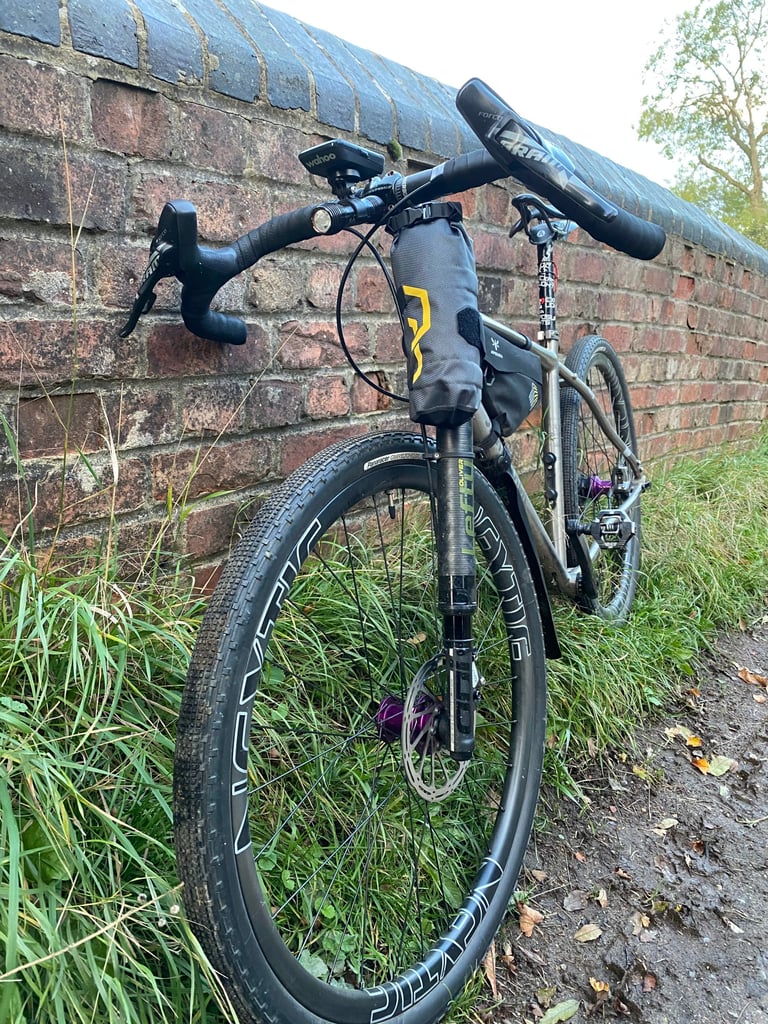 Apidura Downtube Pack strapped to the Cannondale Lefty fork of Tony Clare's bike, beside a brick wall.