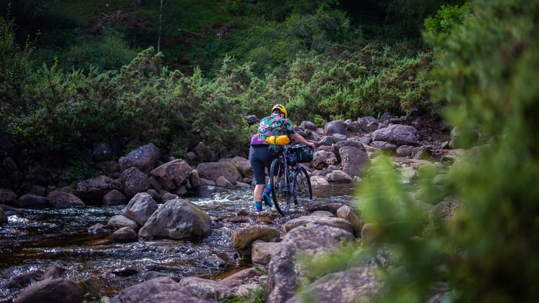 Rider in 7mesh Slab shorts wheels a loaded bikepacking bike across a rocky stream on the Black Mountain, Wales.