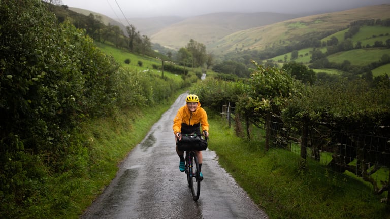 Rider in a yellow jacket rides a wet lane through green Welsh hills on day two of the Storm Ellen overnighter.