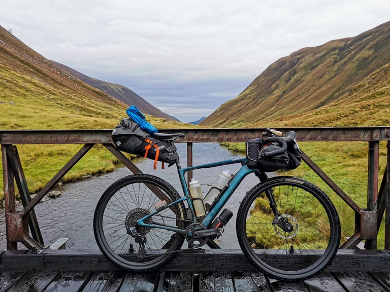 Cannondale Topstone Lefty loaded with bikepacking bags on a rusty bridge over a stream in a Scottish glen.