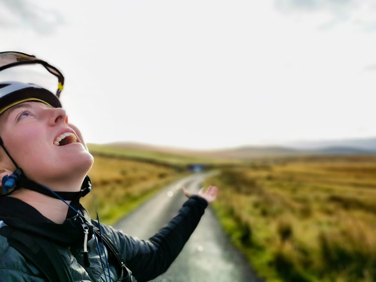 Molly Weaver looks up at the sun with an arm raised on a narrow road across moorland near John O'Groats.