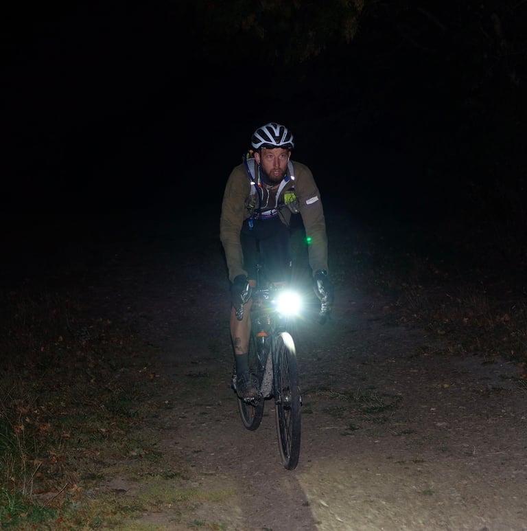 Neil Lauder, Great British Escapade winner, rides at night with a bright front light on a dark track.