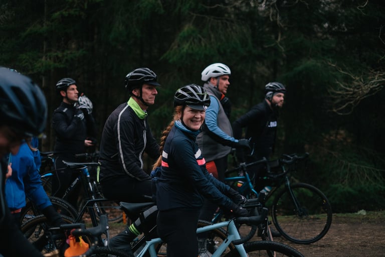 Smiling rider and group in winter kit pause on bikes in woodland before The Woods Cyclery's Sunday ride.