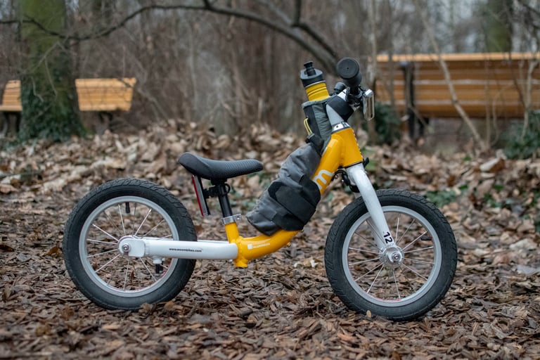Alva Rosenlund's yellow balance bike with an Apidura Downtube Pack strapped to the frame, standing on fallen leaves.