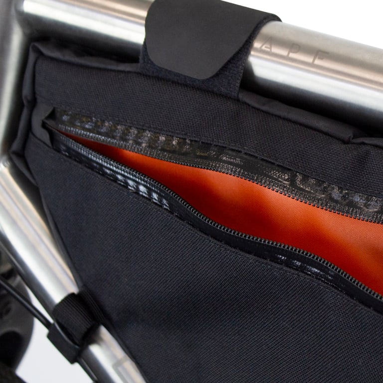 Close-up of a Restrap custom frame bag on a frame tube, with a velcro strap and the zip open to the orange lining.