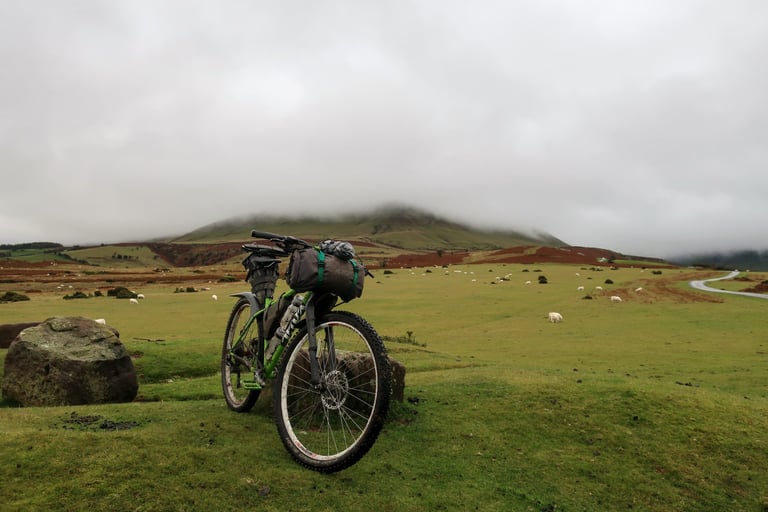 Bikepacking bike on moorland with sheep grazing and cloud covering Hay Bluff in the Brecon Beacons.