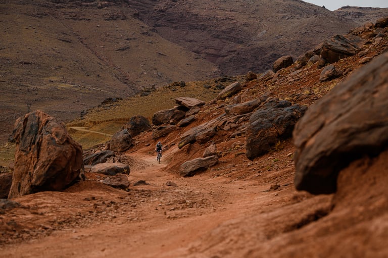 Lone Atlas Mountain Race rider on a rocky red track between boulders in the Moroccan mountains.