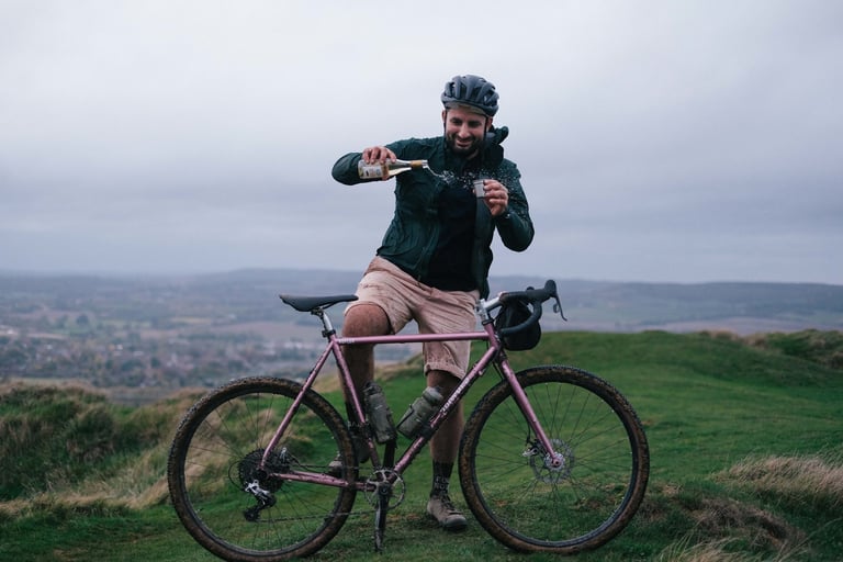 Stef from Pannier pours Muscat into a steel cup astride his pink Brother Kepler on the Wye Downs above the Wye Valley.