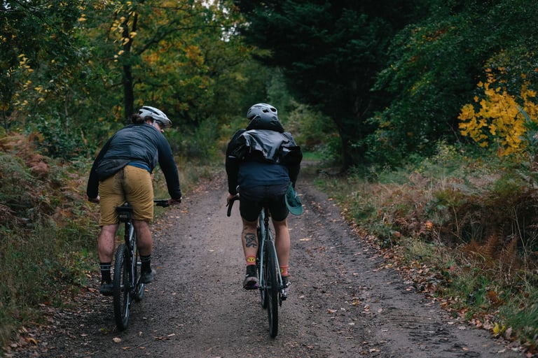Two riders seen from behind on a leaf-covered forest road through Church Wood on the way into Canterbury.