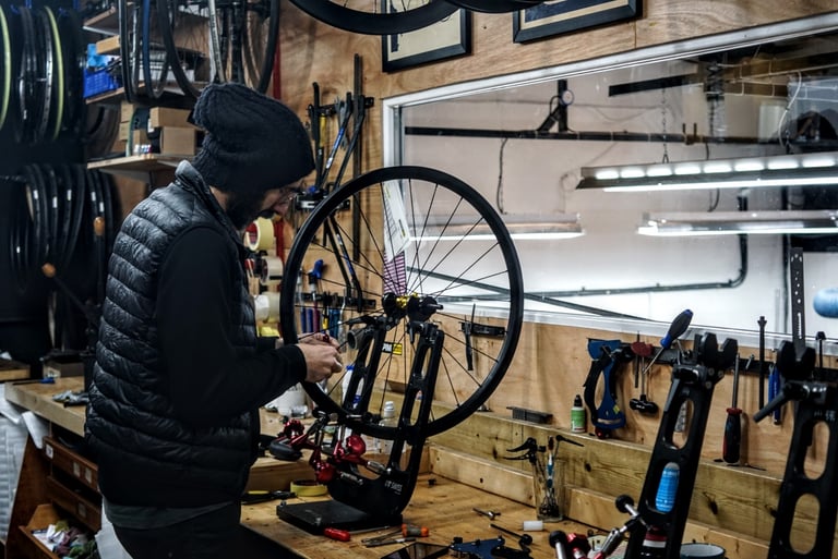 Wheelbuilder in a black gilet truing a wheel in a stand at the Stayer Cycles workshop in Leytonstone.