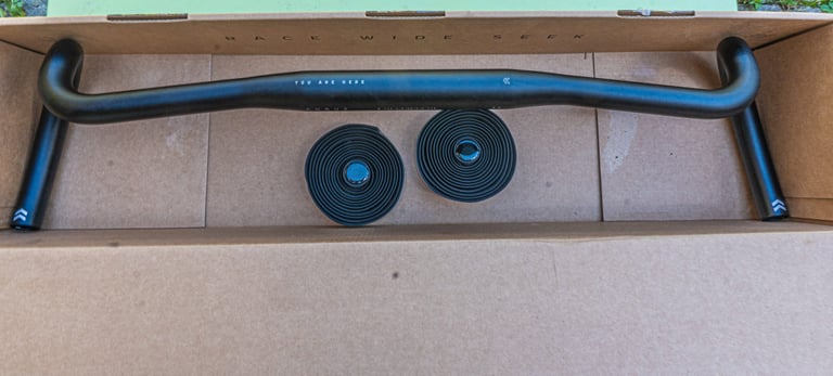 Curve Walmer drop bar and two rolls of bar tape lying in an open cardboard box, showing the wide flared shape.