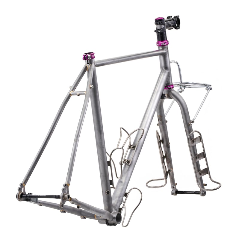 Bare steel Fairlight Faran 2 frameset with fork cargo cages, front rack and purple headset parts, studio shot.