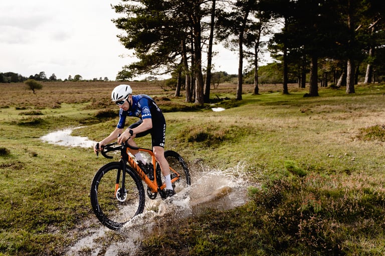 Rider splashes a gravel bike through a puddle on open heathland, on Hunt 42 Limitless Gravel Disc wheels.