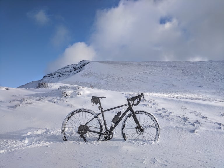 Gravel bike standing in deep snow below a snow-covered mountain under a blue sky.