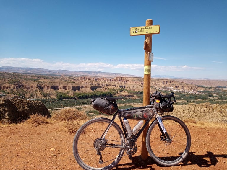 Pelago Sibbo with bivvy bags leans on a signpost to Beas de Guadix above the desert, on the Badlands route.