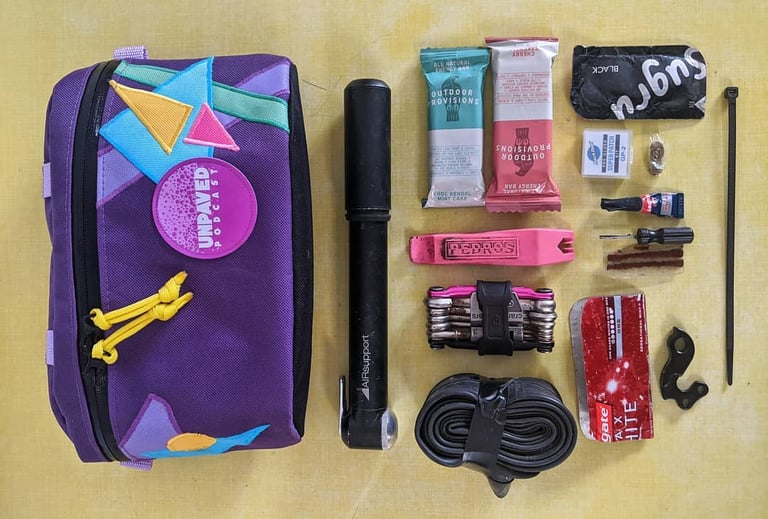 Bike repair kit laid out beside a purple bum bag: pump, tyre lever, multi-tool, spare tube and mech hanger.