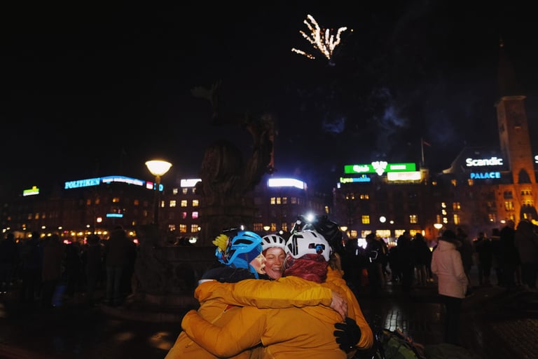 Adventure Syndicate riders hug at night in Copenhagen as fireworks go off at the end of the Resolution Race.