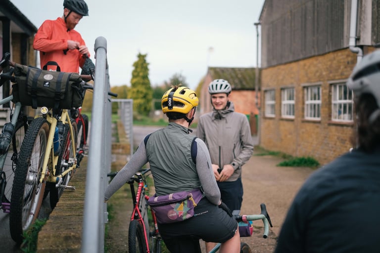Rider in the Velocio Micromodal long sleeve jersey under a gilet, talking to other riders outside a brick building.