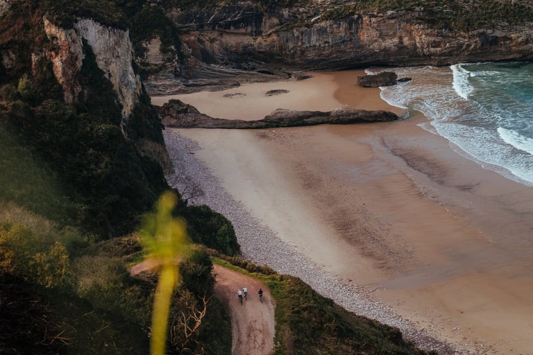 Two riders on a dirt track high above a sandy beach and crashing waves, in a Chris McClean print.