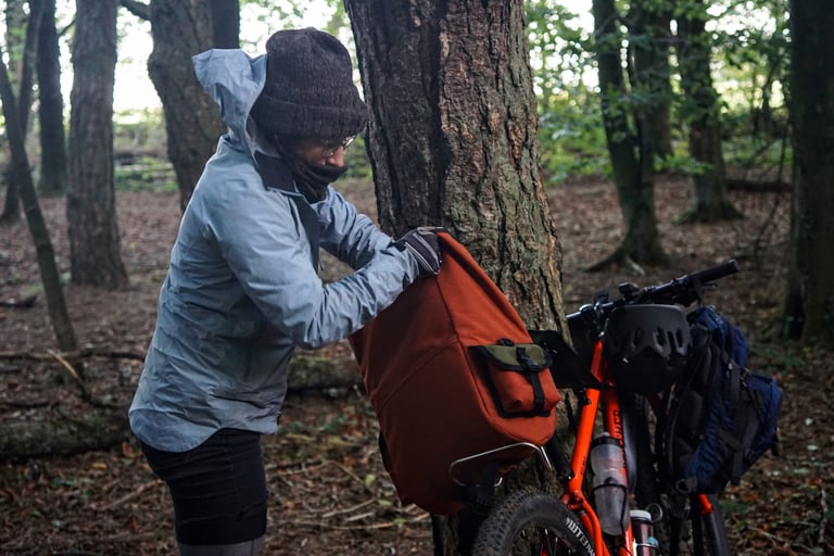 Rider opens the roll-top of the Shazam! saddle bag on an orange bike beside a tree in woodland.