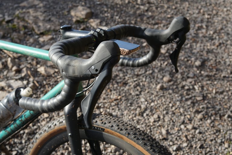 Close-up of Shimano GRX levers and black silicone bar tape on the Stayer Groadinger UG, with a Teravail tyre below.