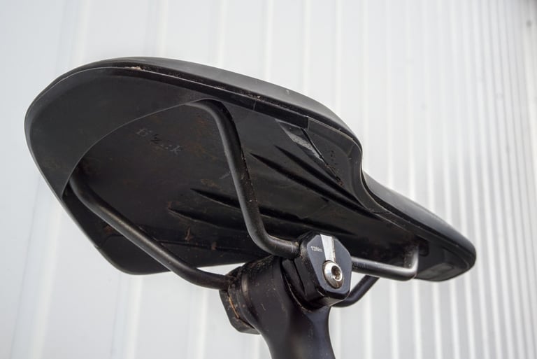 Underside of the Fizik Terra Argo X3 saddle on a seatpost, showing the shell and rails with some trail dirt.