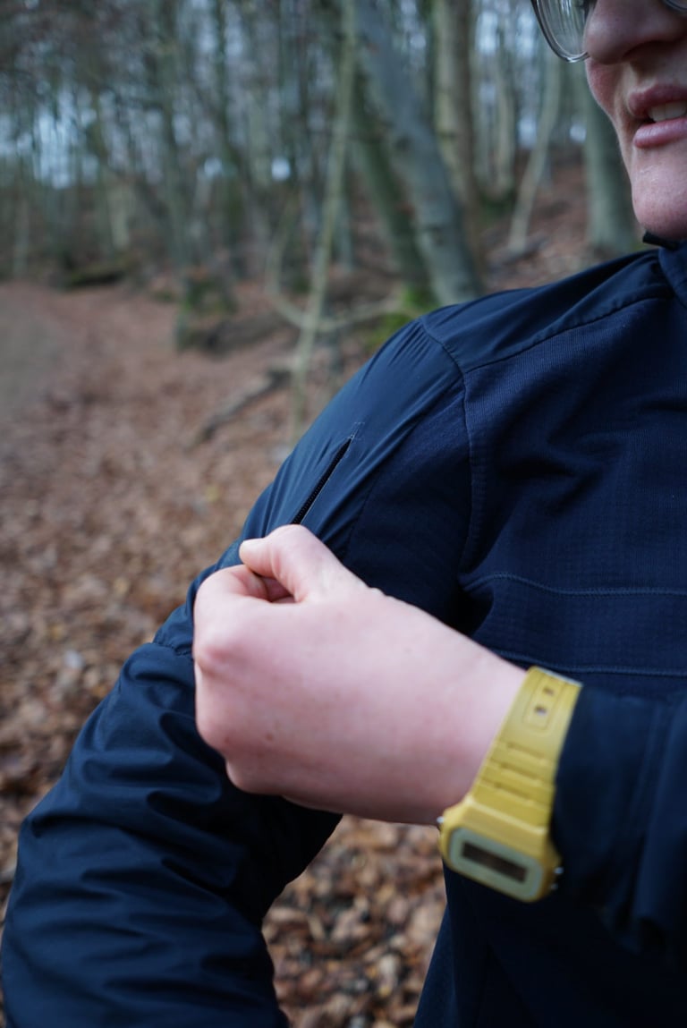 Rider's hand beside the zipped upper-arm pocket in the windproof panel of the Rapha Explore Long Sleeve Pullover.