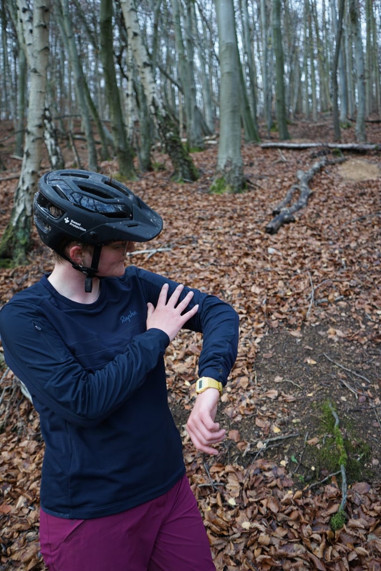 Rider grips the windproof upper-sleeve panel of the Rapha Explore Long Sleeve Pullover in beech woodland.