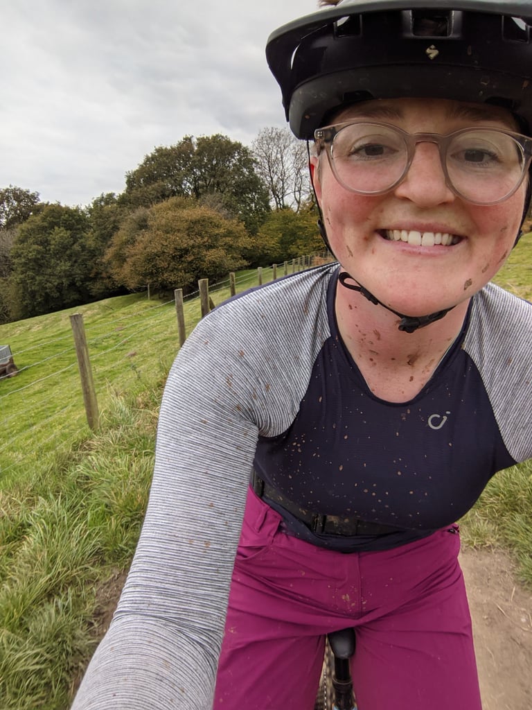 Mud-spattered selfie of a rider in the Velocio Micromodal long sleeve jersey and magenta baggies beside a field.