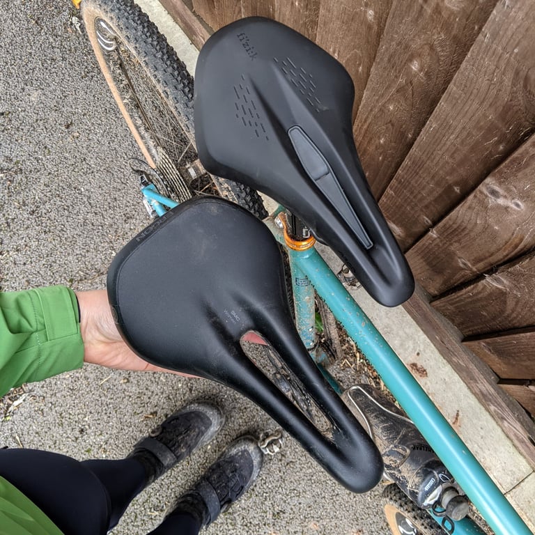 Fizik Terra Argo X3 fitted to a teal gravel bike, with the Ergon SMC Women saddle it replaced held alongside.