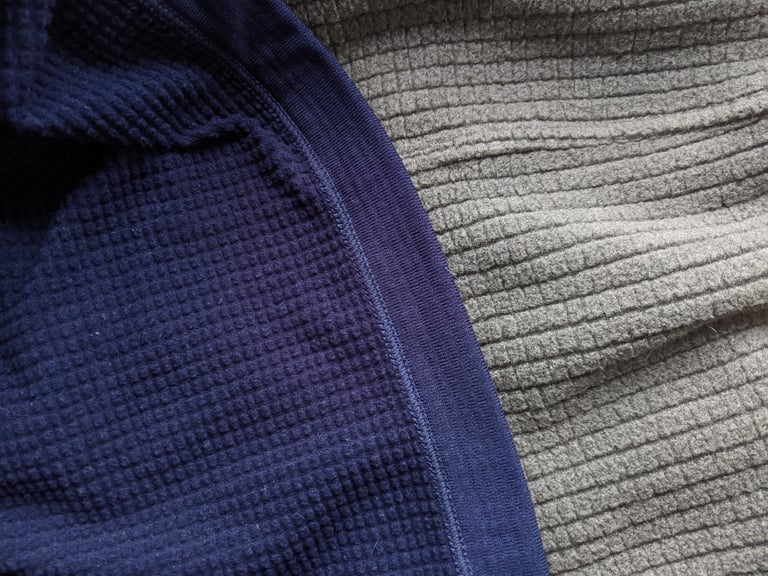 Fine navy grid fleece of the Rapha Explore pullover beside the coarser grey grid of the original Explore Fleece.