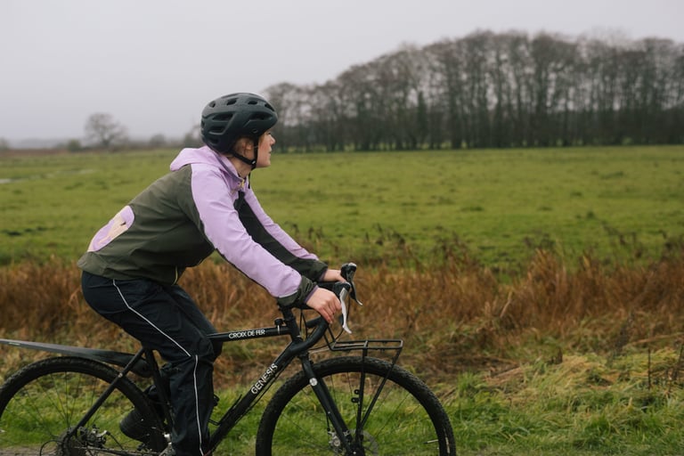 Rider in the IRIS Escape Jacket pedals a Genesis Croix de Fer past wet fields on a grey winter day.