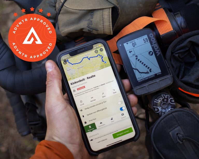 Wahoo ELEMNT ROAM on a loaded handlebar beside a phone showing a komoot route near Raalte in the Netherlands.