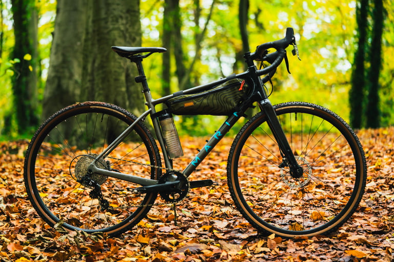 Marin Headlands gravel bike with 38 mm Panaracer GravelKing EXT Plus tyres, parked on autumn leaves in woodland.