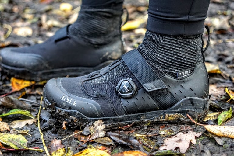Fizik winter cycling boots with Boa dials, caked in mud among fallen leaves on an off-road ride.