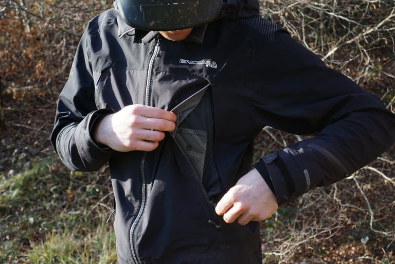Rider opens a large mesh-lined front pocket on the Endura MT500 Waterproof Jacket II, which doubles as a vent.