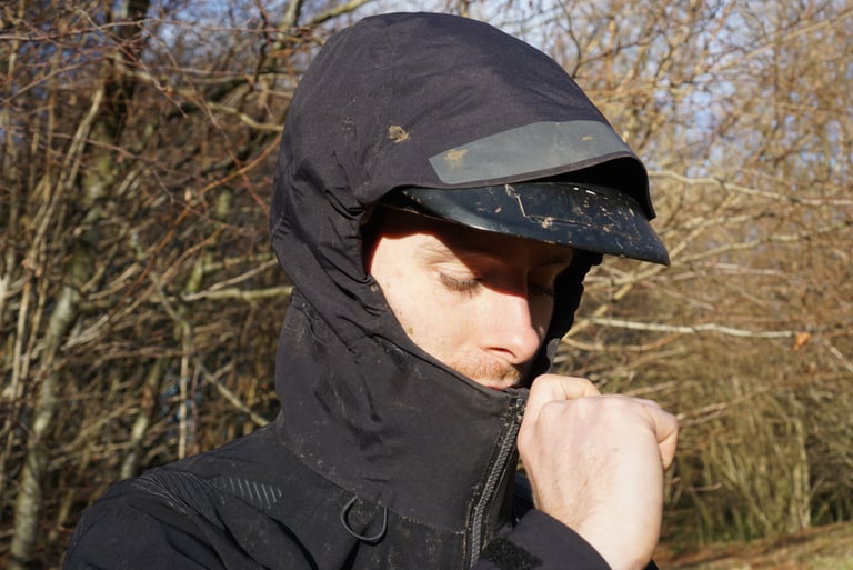 Close-up of the Endura MT500 Waterproof Jacket II hood pulled over a peaked helmet as the rider zips it up.