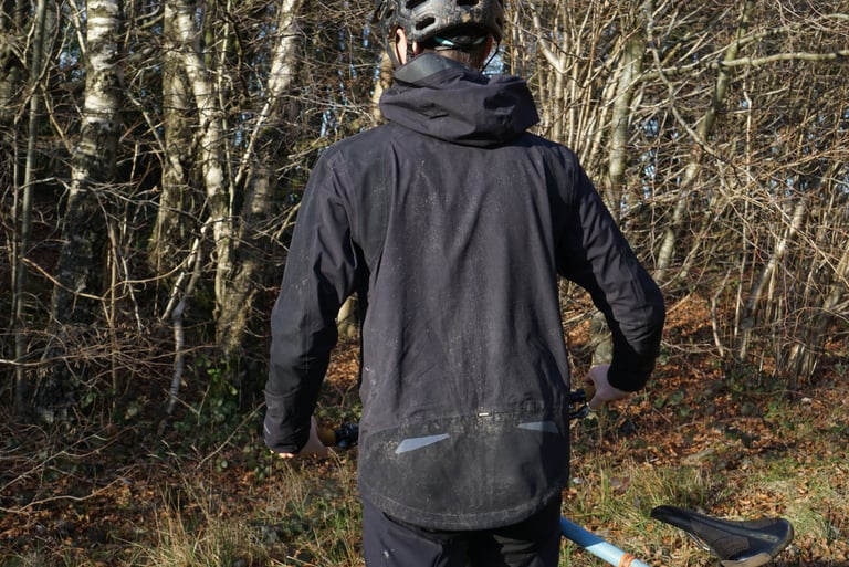 Rear view of the mud-flecked Endura MT500 Waterproof Jacket II showing its dropped hem and reflective detailing.