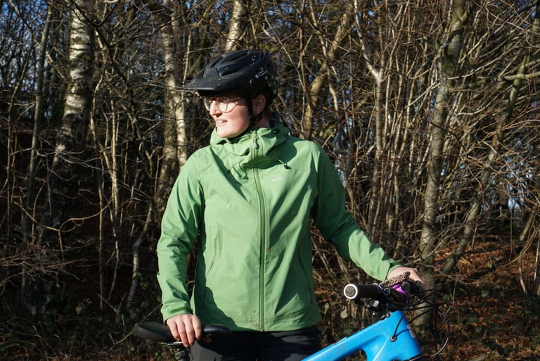 Alpkit Balance waterproof jacket in Fern Green on a rider holding a mountain bike, showing the mid-length fit.