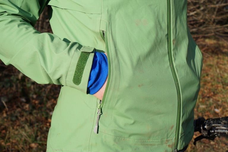 Close-up of an Alpkit Balance chest pocket with zip toggle and velcro cuff strap, a hand tucked inside.