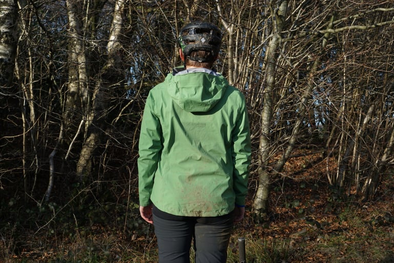 Back of the Alpkit Balance jacket showing the slightly dropped hem and hood, worn with a helmet in winter woodland.