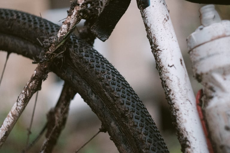 Mud-caked Halo GXC gravel tyre with diamond-pattern tread beside a muddy white frame and bottle.
